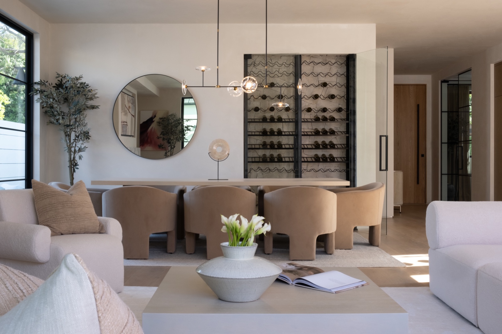 Sophisticated dining space featuring a modern chandelier, rounded upholstered dining chairs, and a floor-to-ceiling custom glass wine display wall.