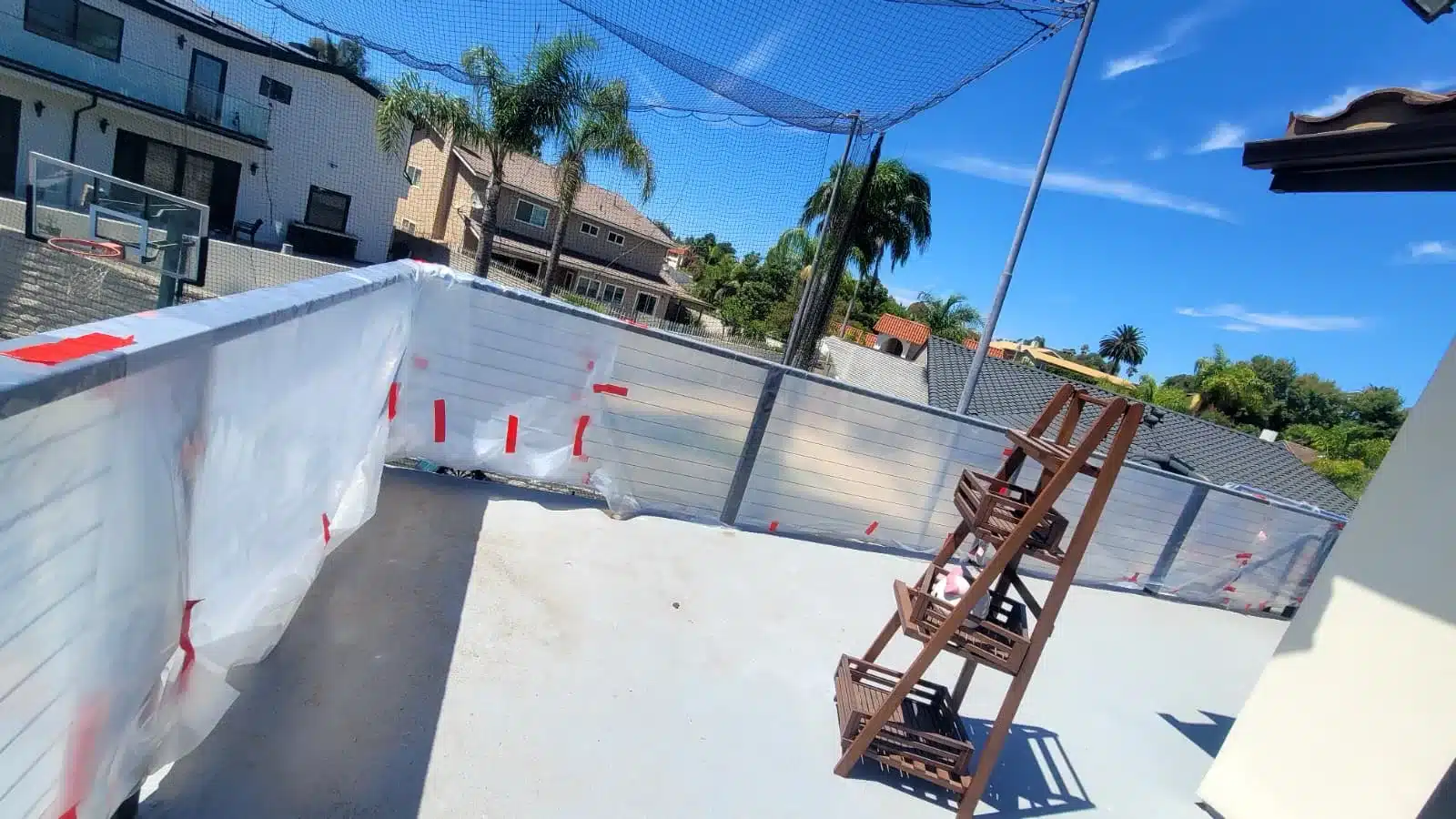 Open deck with plastic-covered perimeter walls and a wooden plant stand beneath overhead netting.