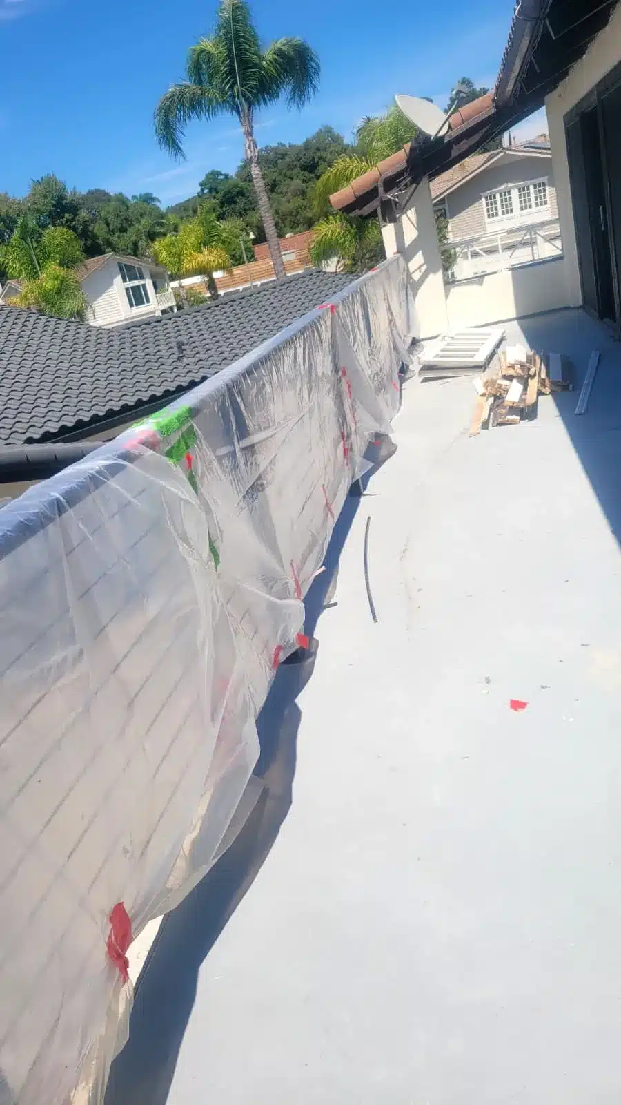 Narrow exterior deck with plastic-covered railing, stacked construction materials and an adjacent dark tiled roof.