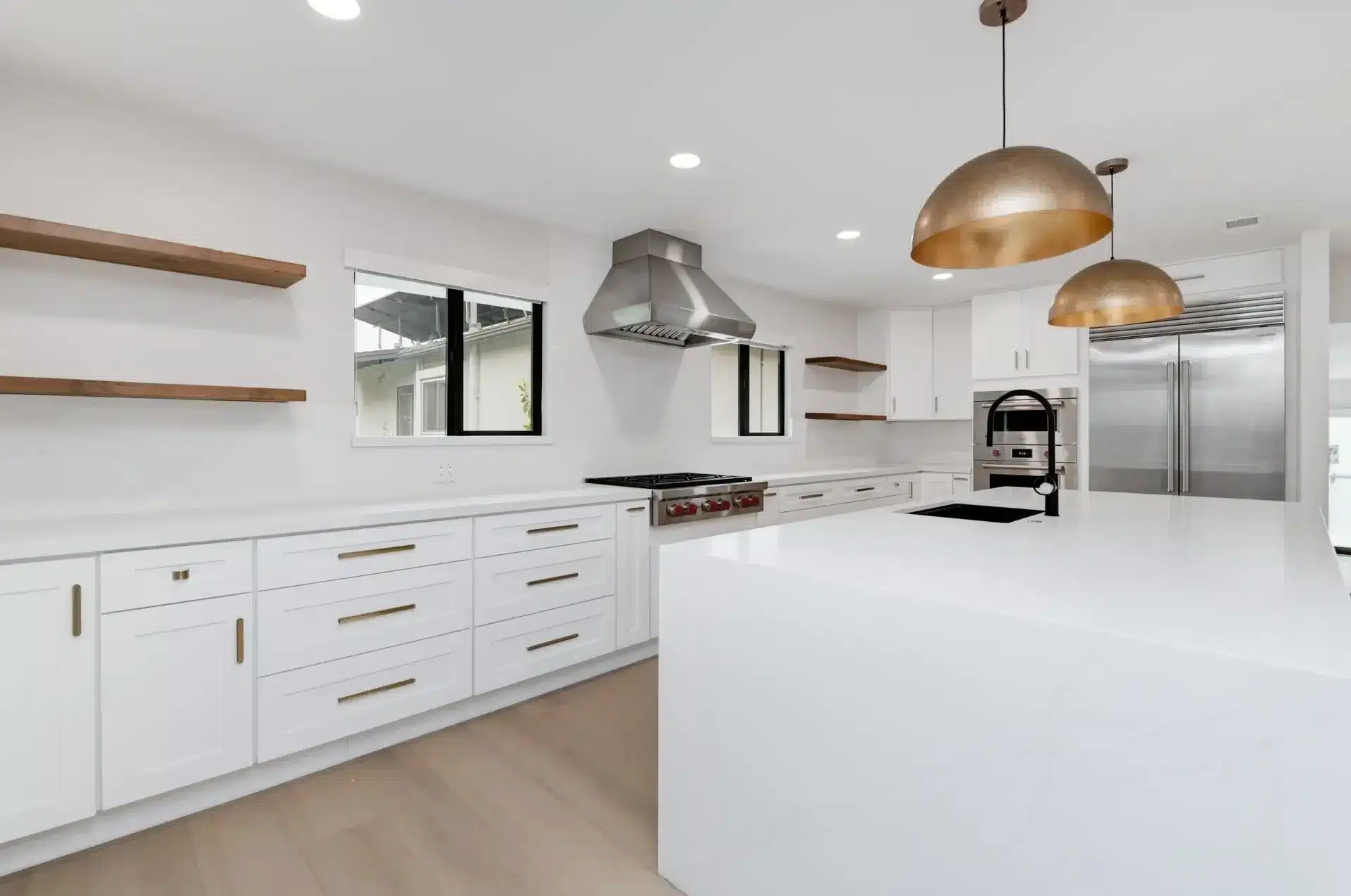 Modern kitchen with white cabinetry, large white island, stainless steel appliances, and brass pendant lights