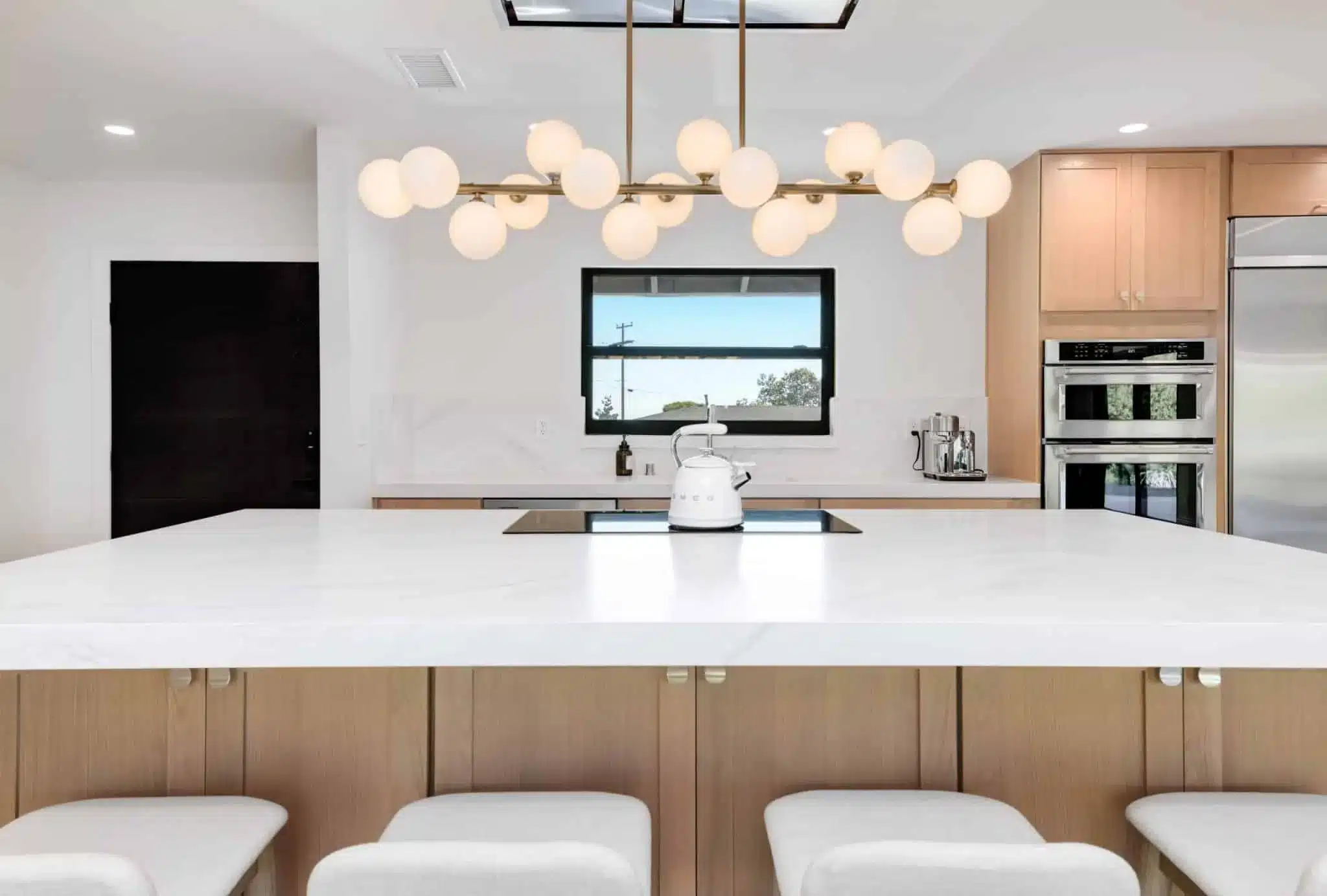 Modern kitchen with white countertop, light wood cabinets, double ovens, and brass pendant lights above island.
