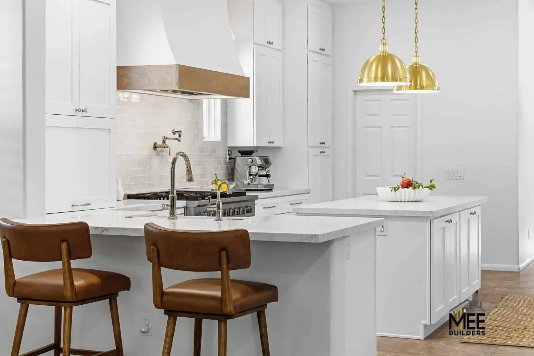 Modern kitchen with white cabinets, quartz countertops, large island, gold pendant lights, and brown leather bar stools