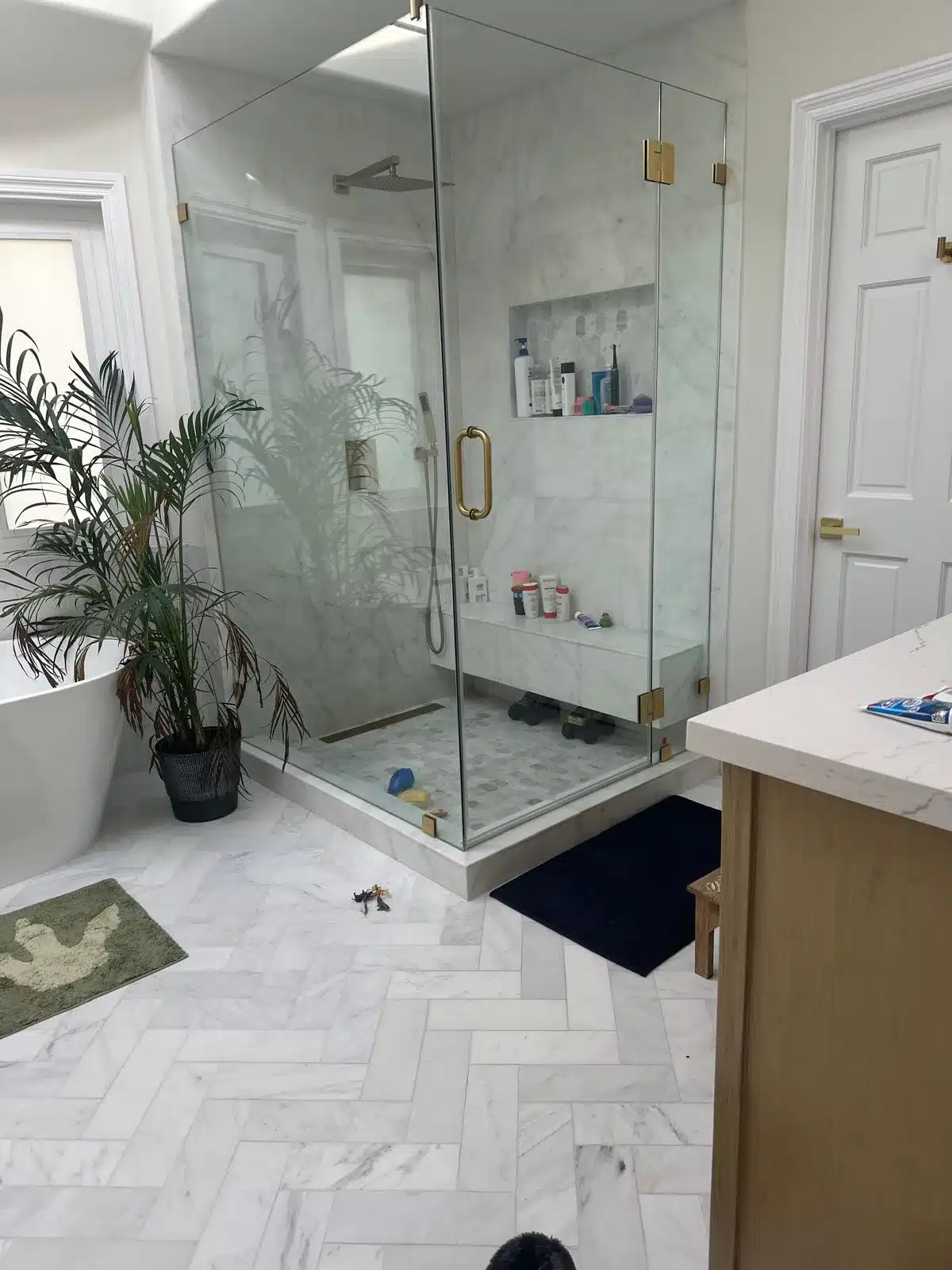 Finished bathroom with frameless glass shower, marble tile, built-in bench, and light wood vanity.