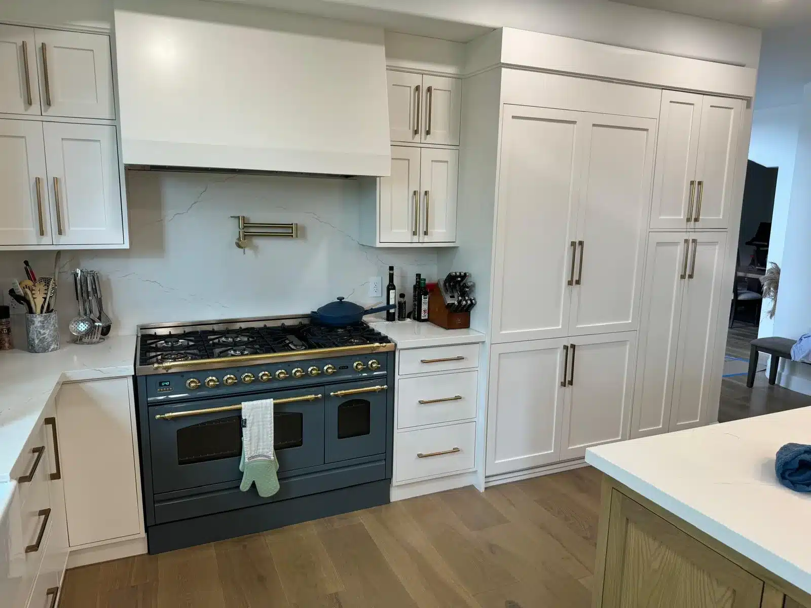 Finished cooking wall with a dark blue range, gold-colored accents, white hood, and tall shaker-style cabinetry