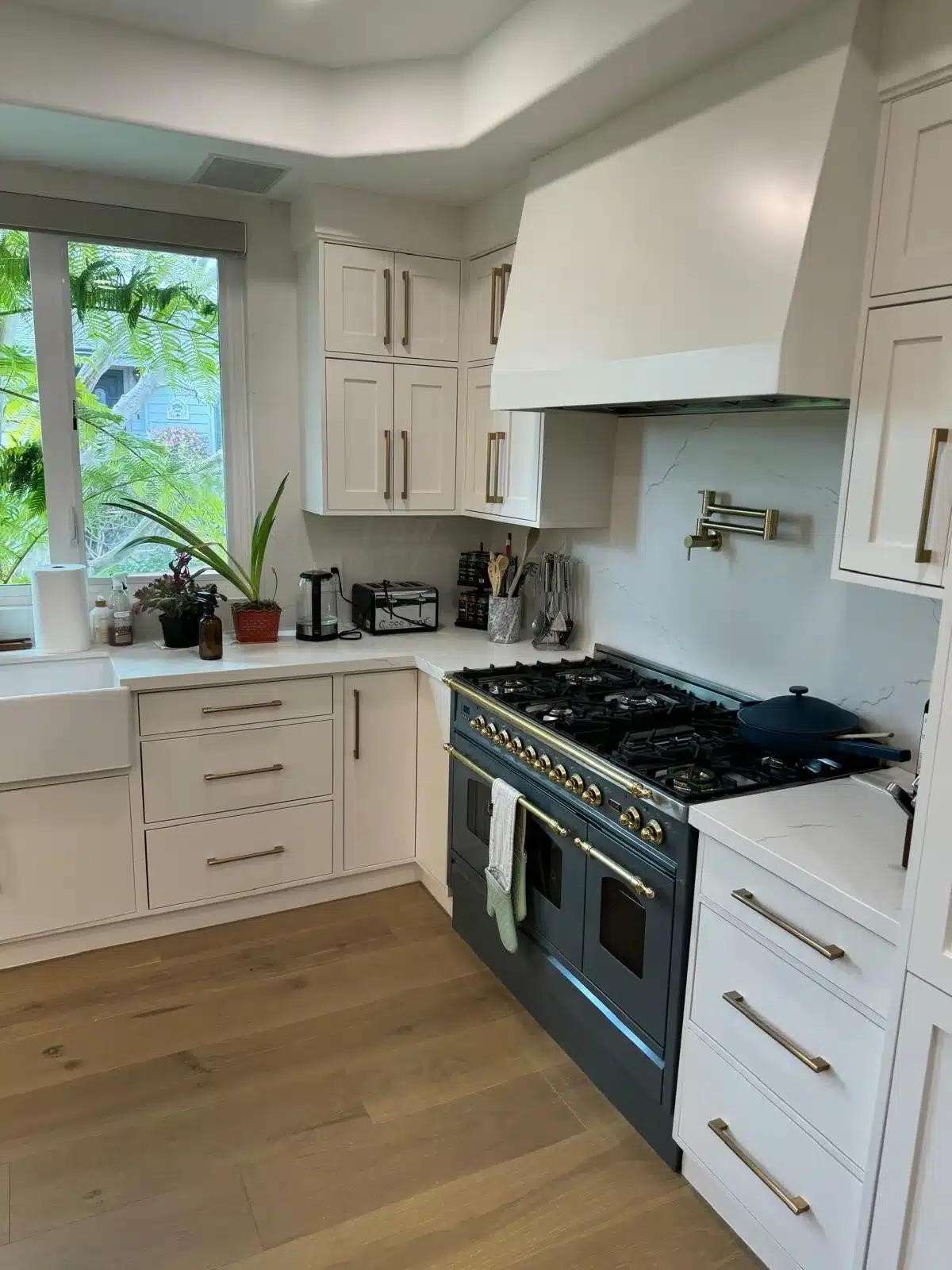 Finished kitchen corner with an apron-front sink, window overlooking foliage, veined backsplash, and dark range