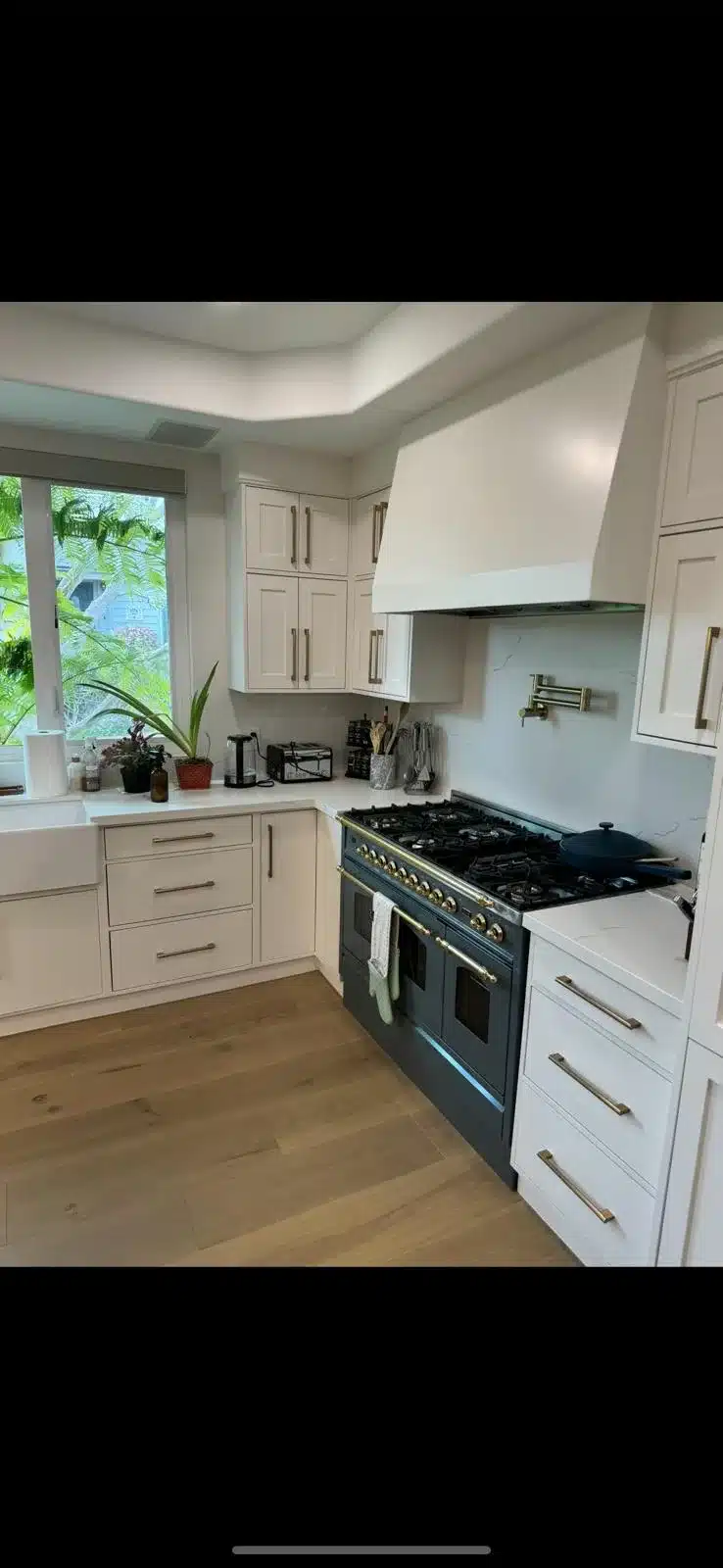 Finished kitchen with light cabinets, a white range hood, pale veined counters, and warm wood flooring
