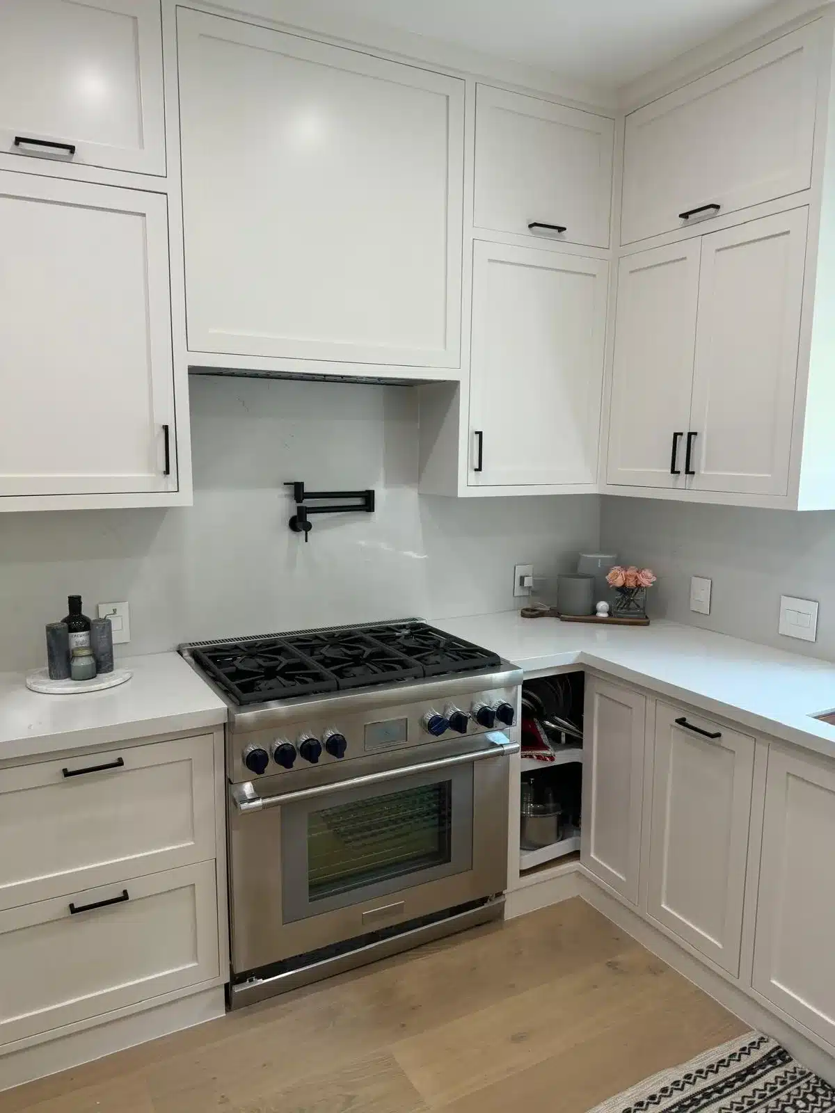 Finished kitchen cooking area with a stainless steel gas range, black pot filler, and open corner cabinet.