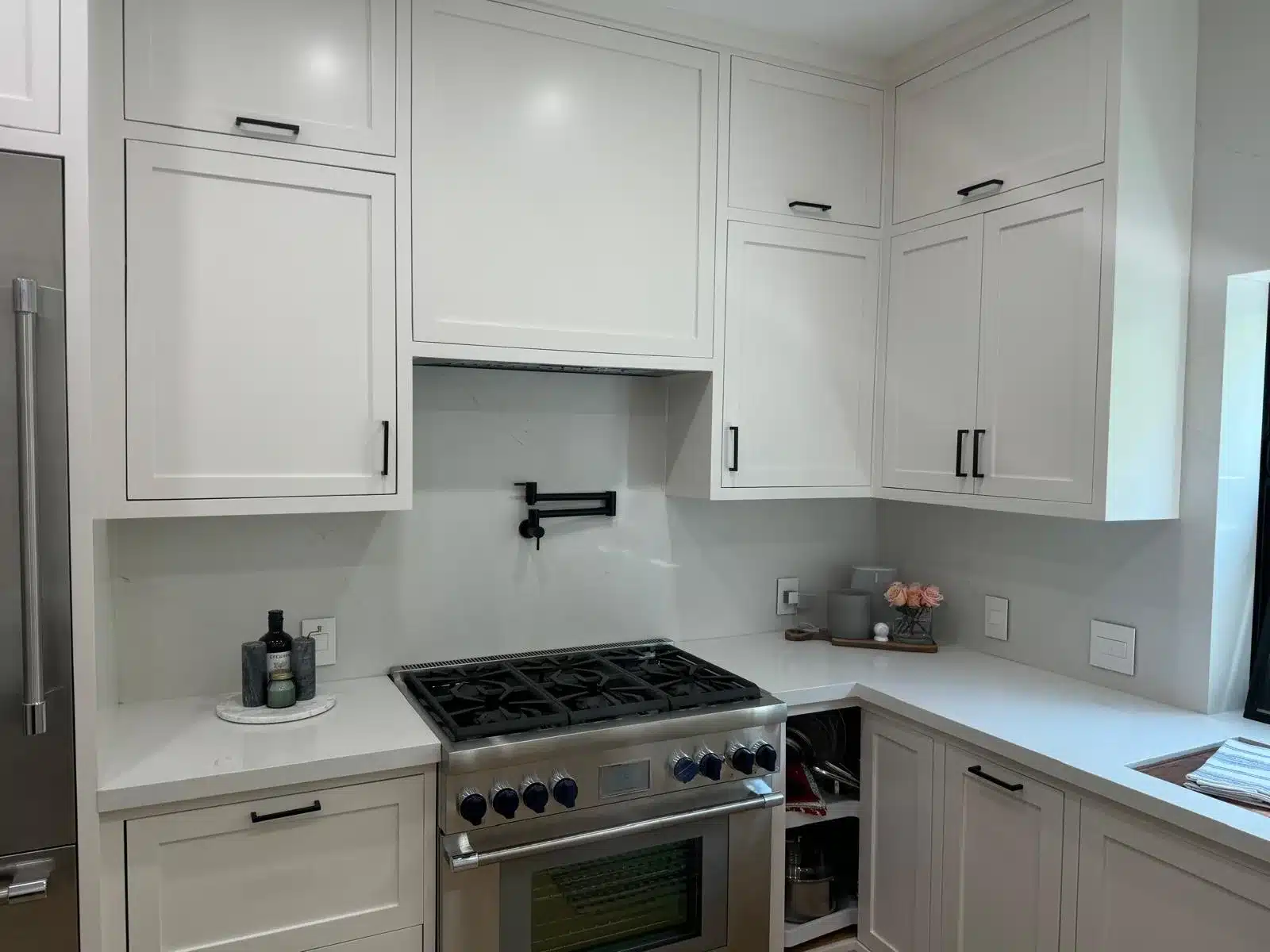 Finished range wall with white shaker-style cabinets, black pulls, and a pale veined backsplash.