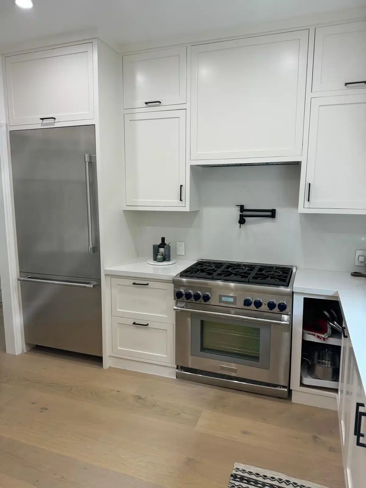 Finished kitchen with stainless steel refrigerator and range, white cabinetry, and light wood-toned flooring.