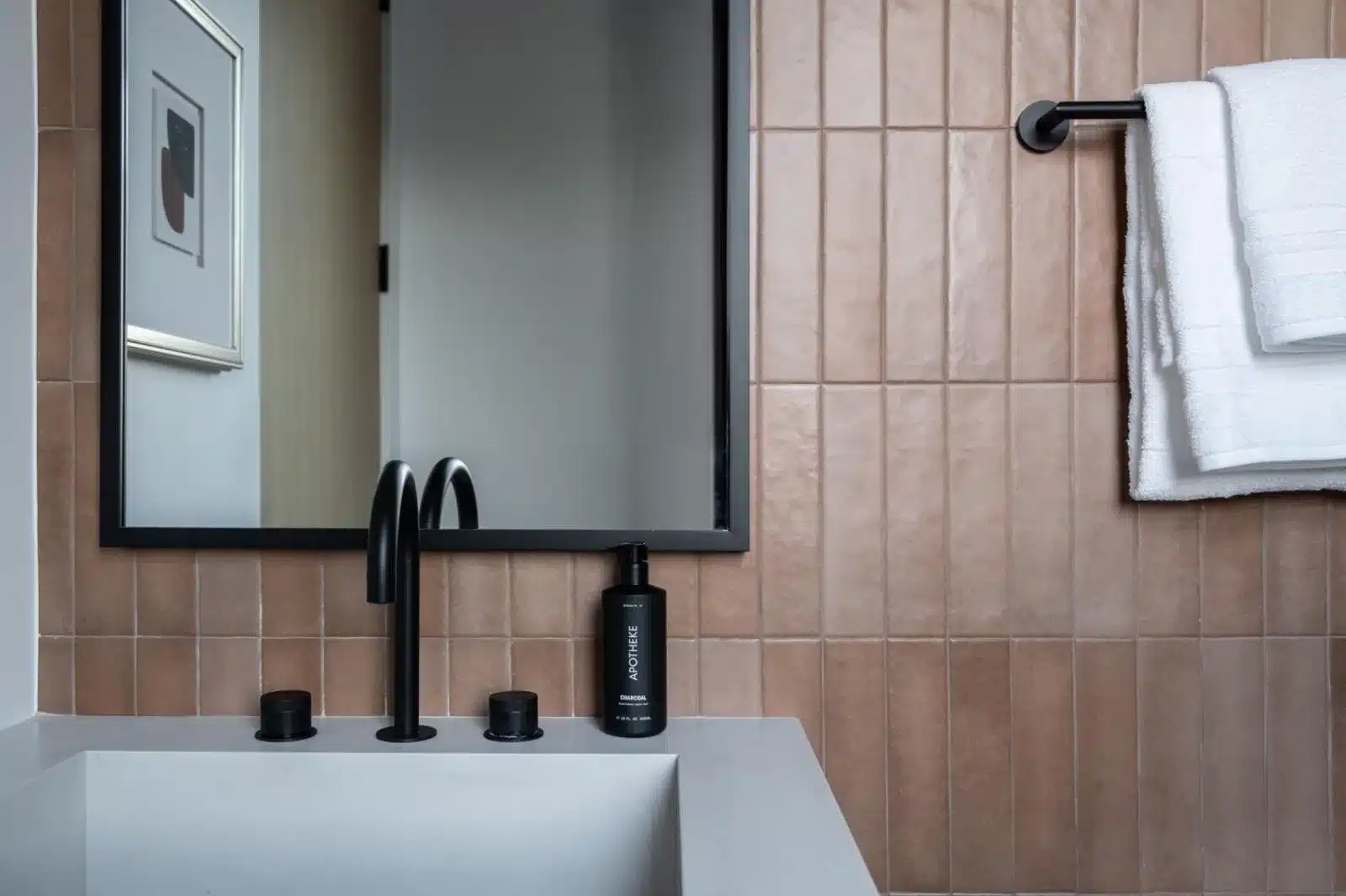 Finished bathroom vanity with a white sink, black faucet and mirror frame, and warm brown vertical wall tile