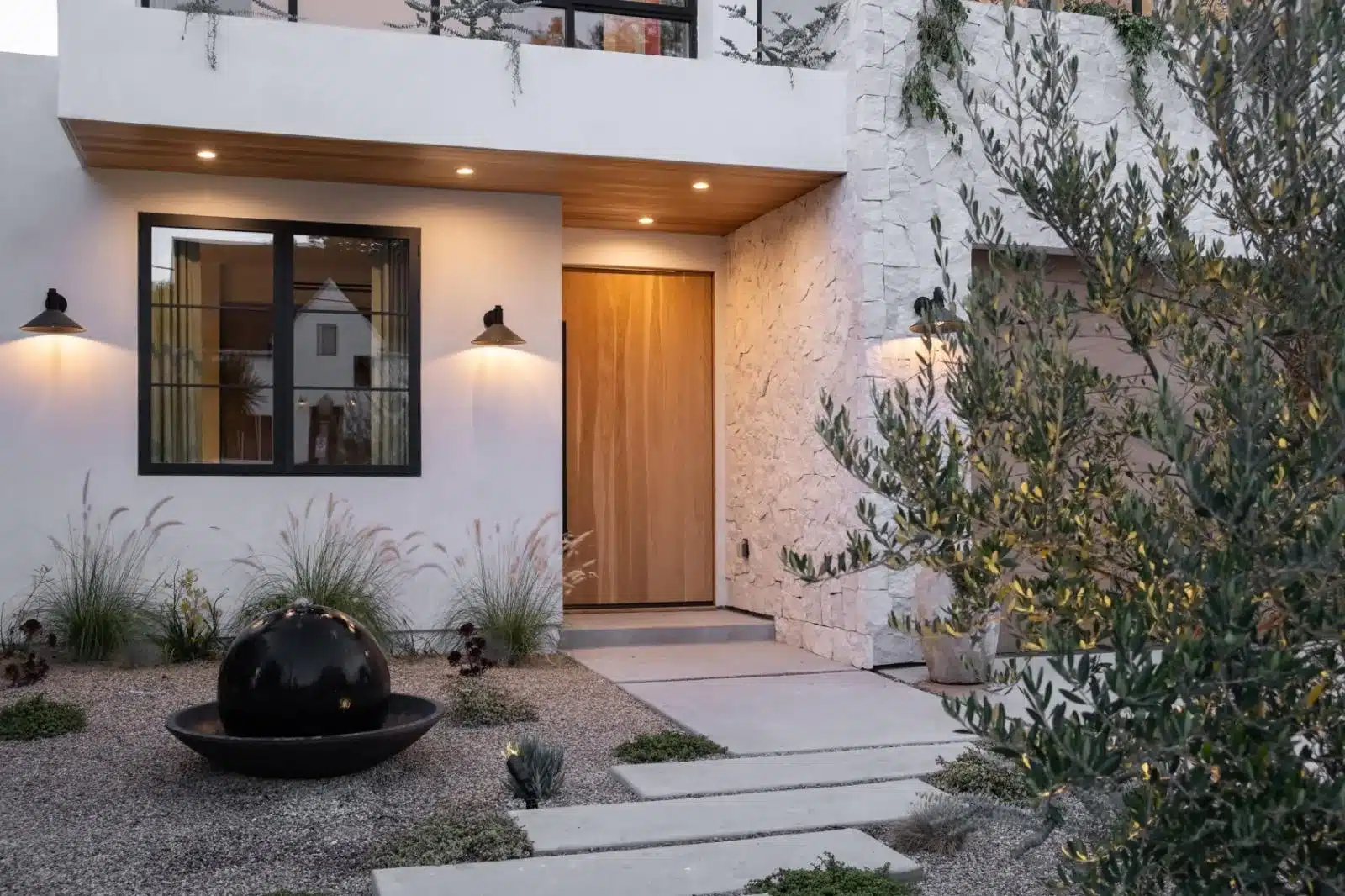 Finished entry with a wood door, recessed lighting, concrete stepping stones, gravel planting beds, and a black spherical