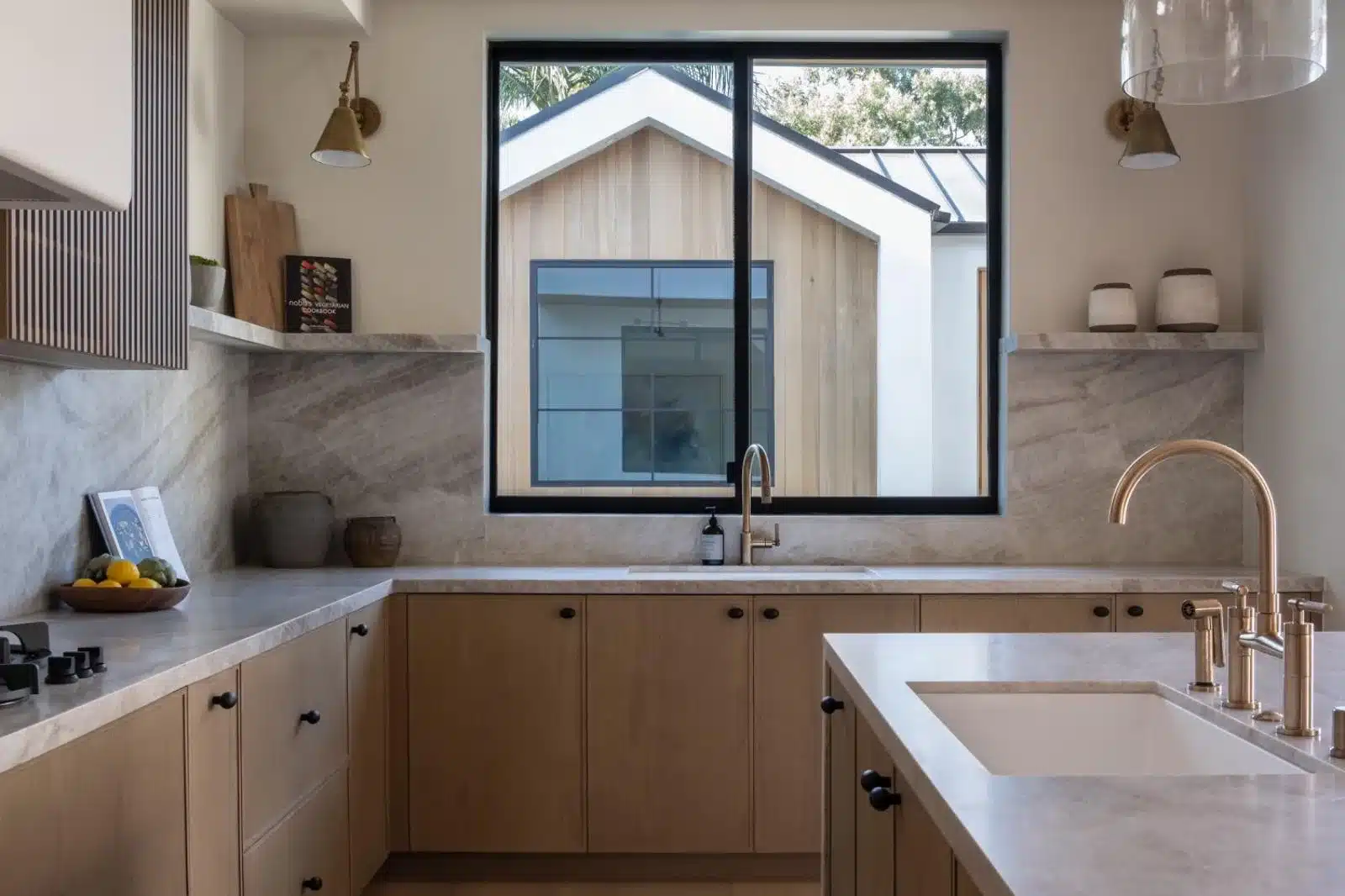 Finished kitchen with light wood cabinets, black hardware, veined counters, and a sink beneath a black-framed window