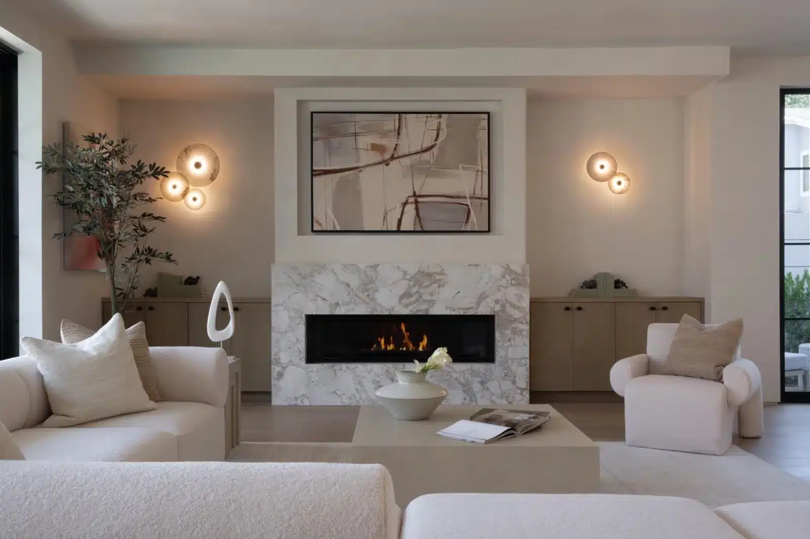 Finished living room with a veined fireplace surround, built-in wood cabinets, cream seating, and wall lights