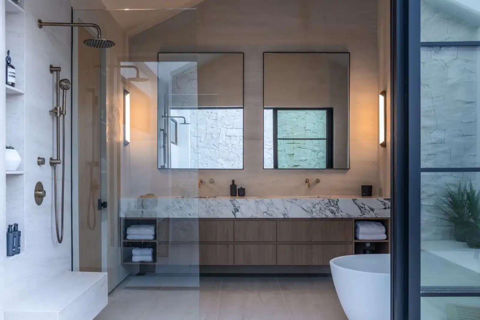 Finished bathroom with a veined vanity top, wood drawers, framed mirrors, glass shower enclosure, and freestanding tub