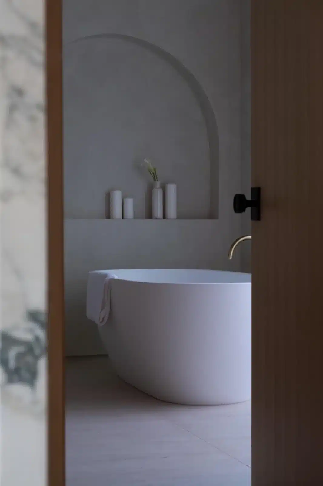 Finished bathroom detail showing a curved white tub beneath an arched wall niche with candles and a vase