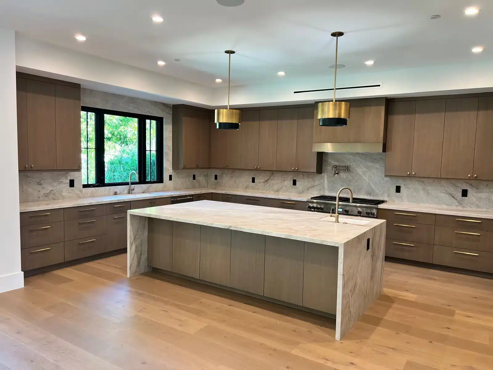 Finished kitchen with wood cabinetry, a veined waterfall-edge island, brass-toned pendants