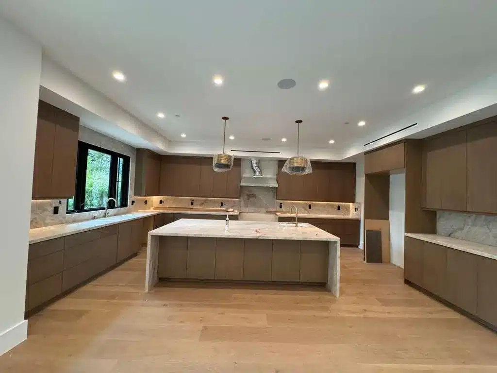 Kitchen during finishing work with covered pendant lights, wood cabinetry, a waterfall-edge island, and an empty