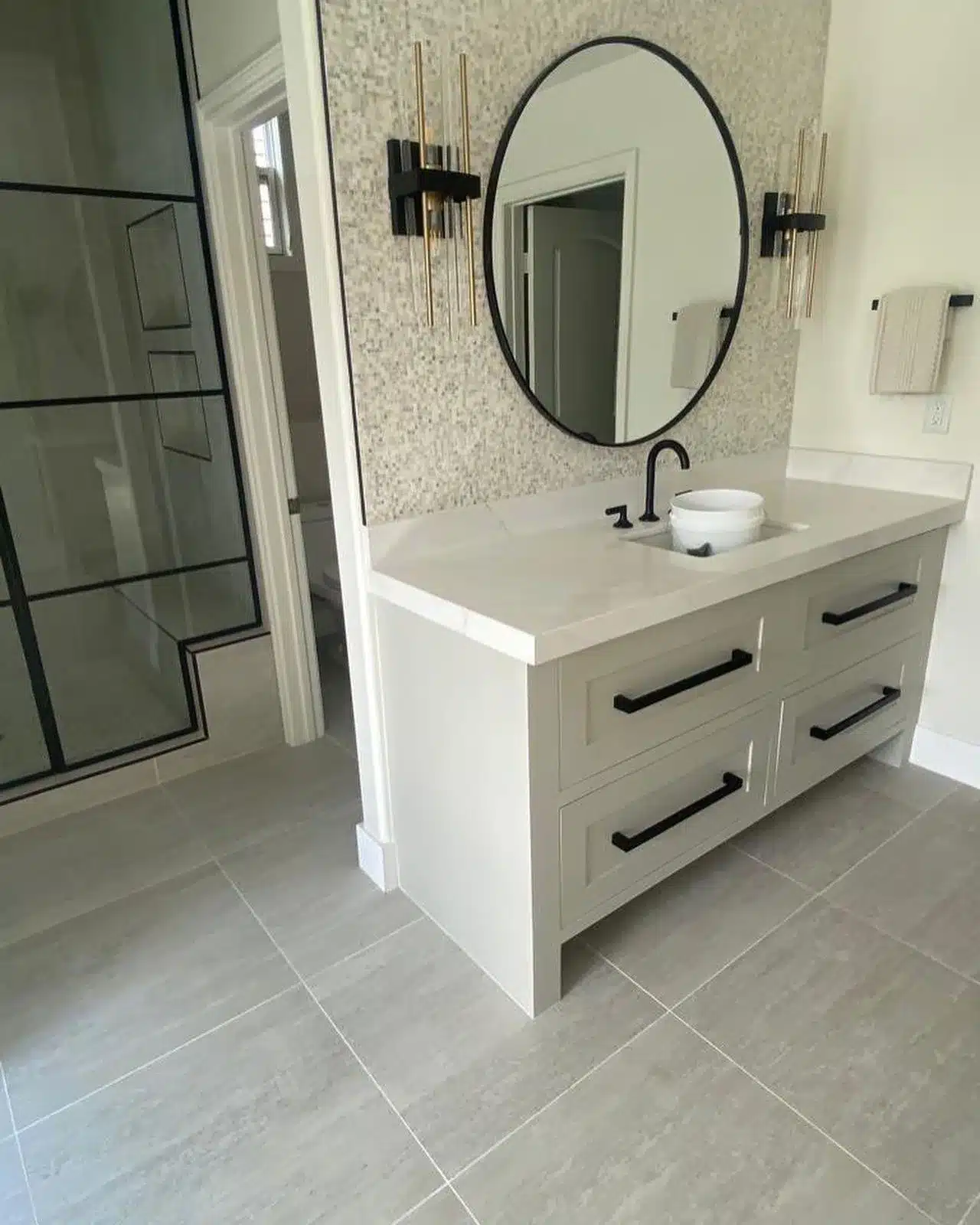 Installed vanity and mosaic backsplash beside a glass shower enclosure with dark geometric trim.