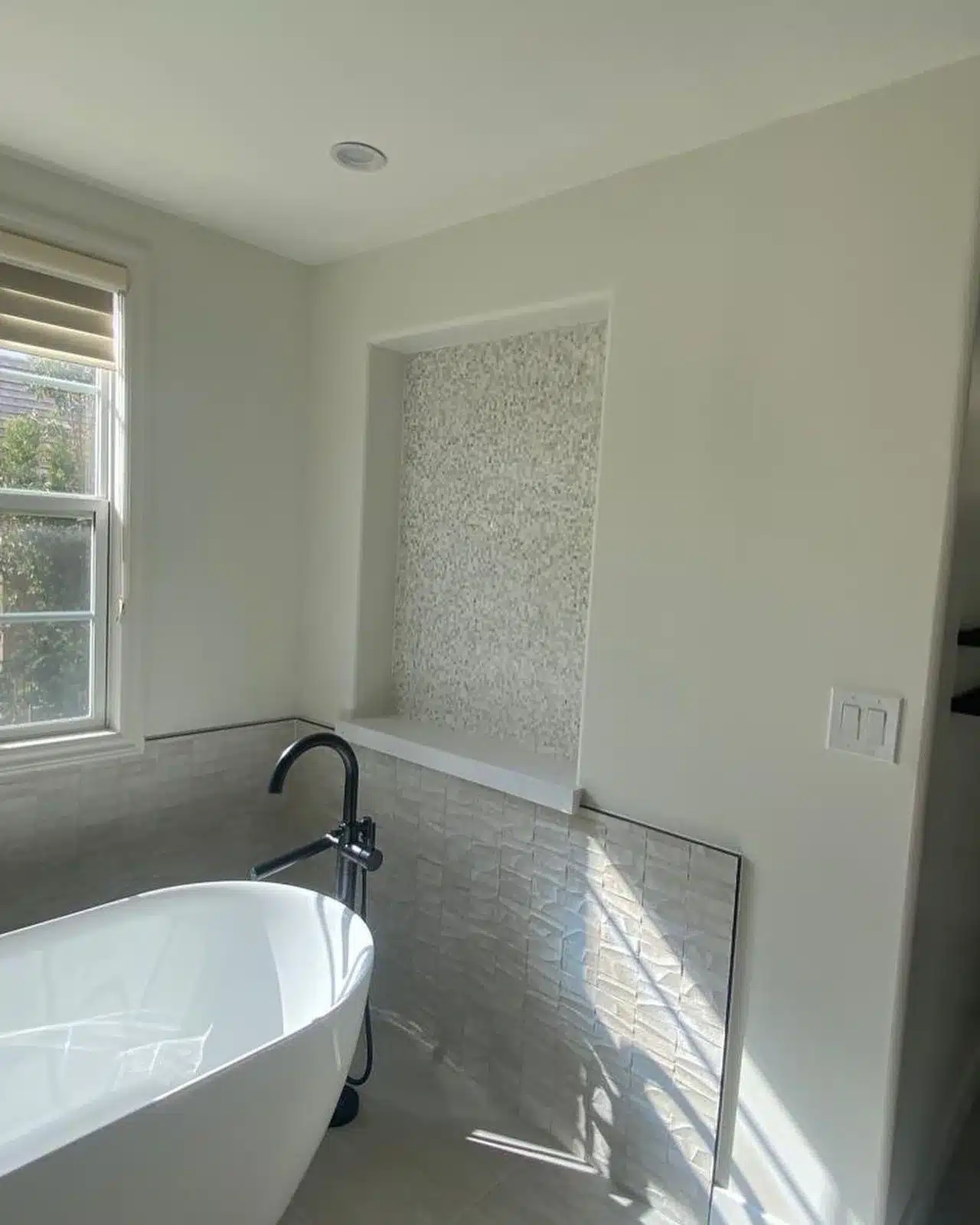 Finished tub area with a recessed mosaic-tile panel, textured lower-wall tile, and black tub filler.