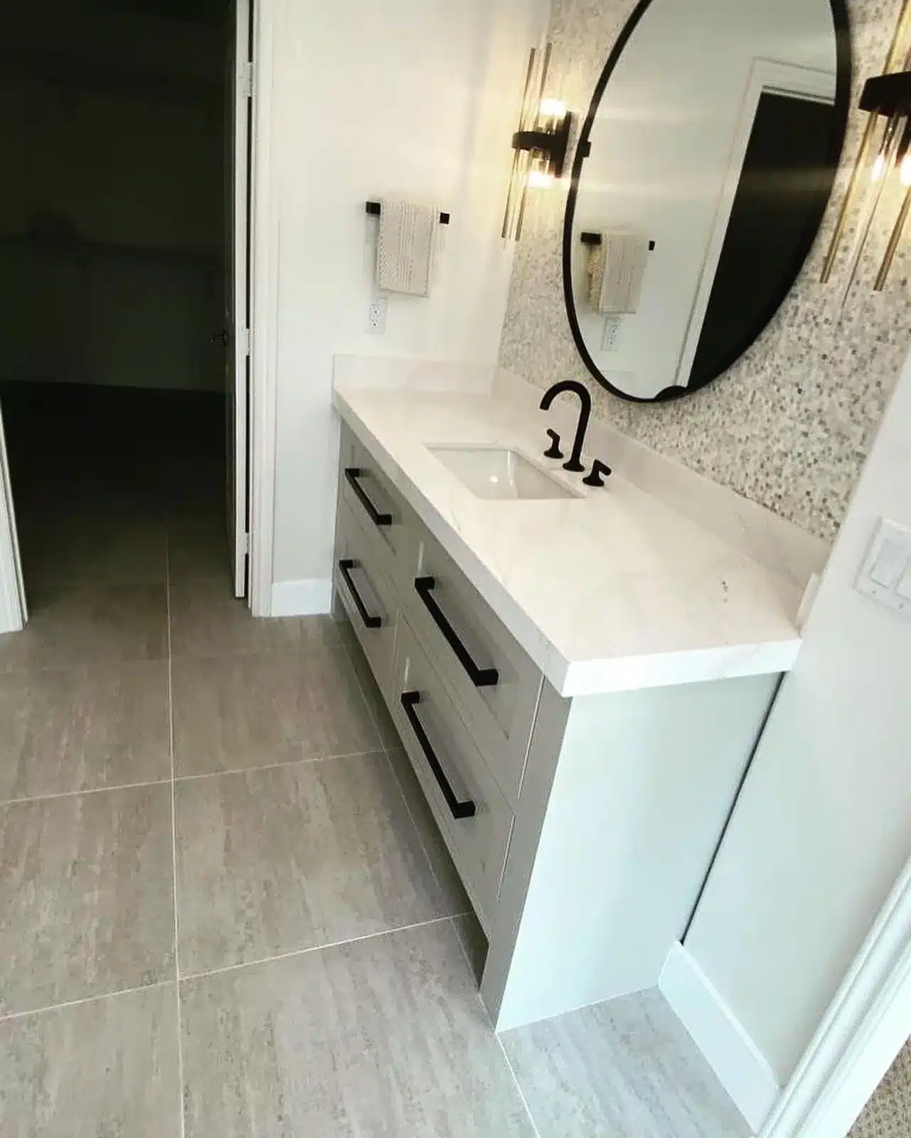Finished vanity with paneled drawers, long black pulls, a round black-framed mirror, and wall sconces.