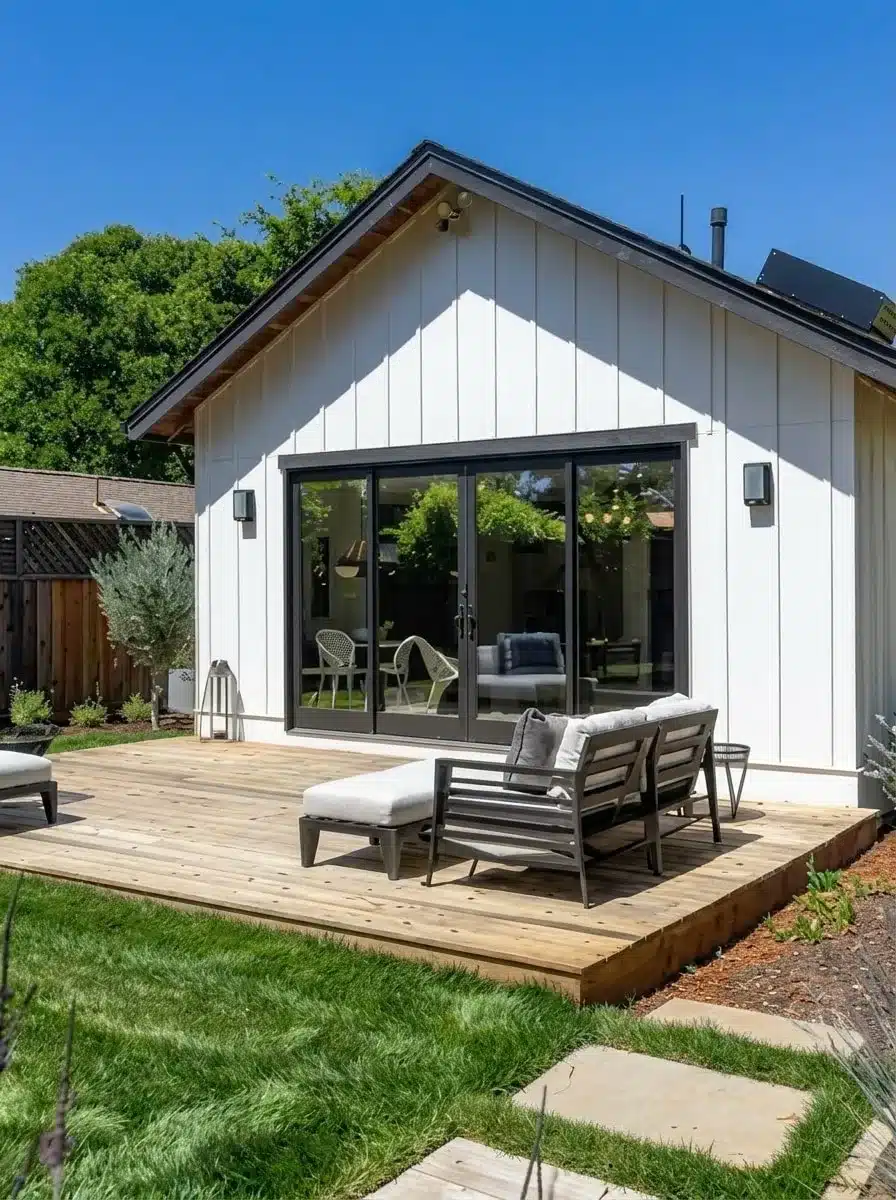 Detached backyard ADU with black-framed glass doors set back from the property line behind a wood deck